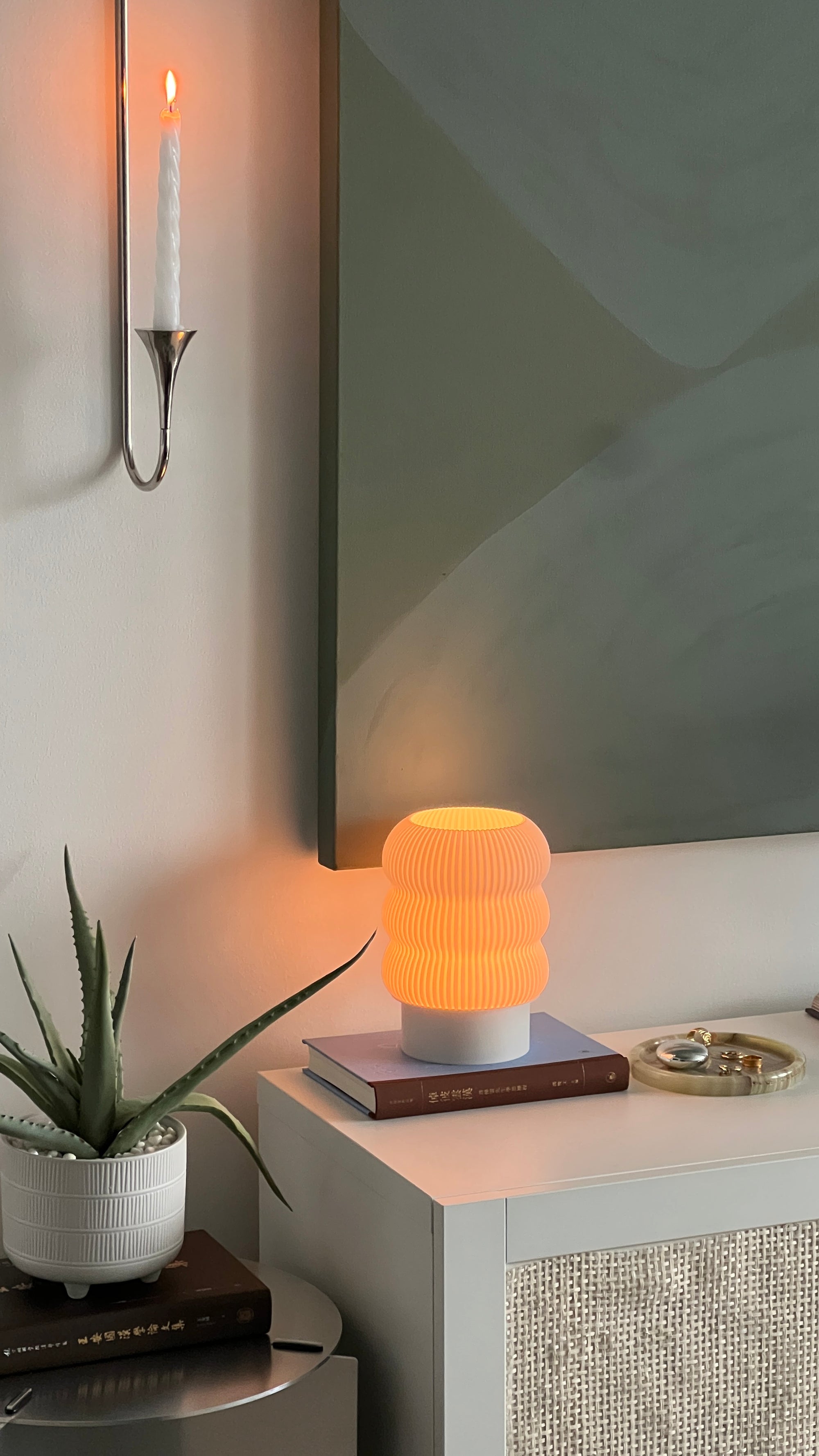 Small table lamp on a nightstand with a plant and mirror in the background