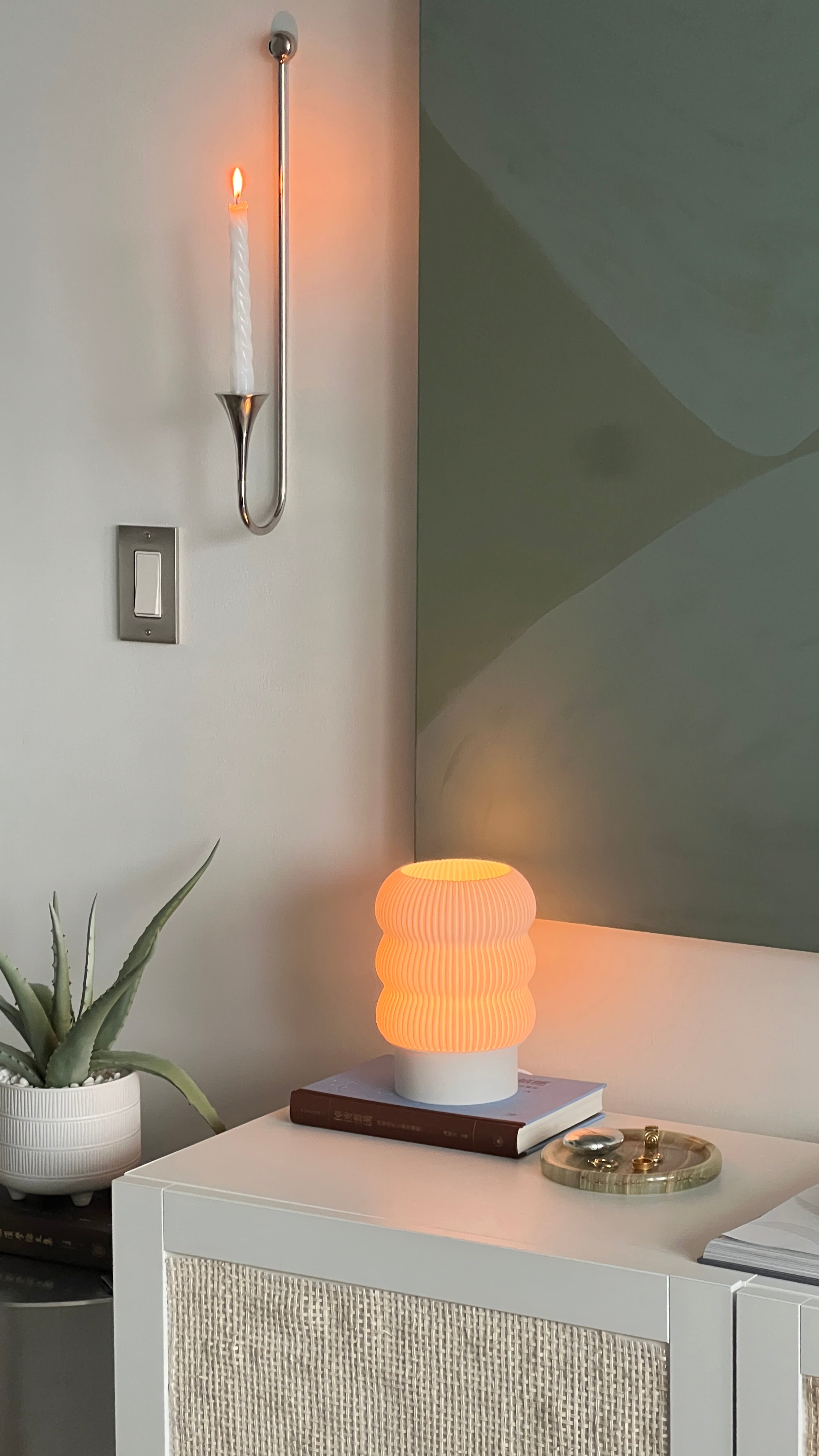 Small table lamp on a surface with a candle and plant in the background