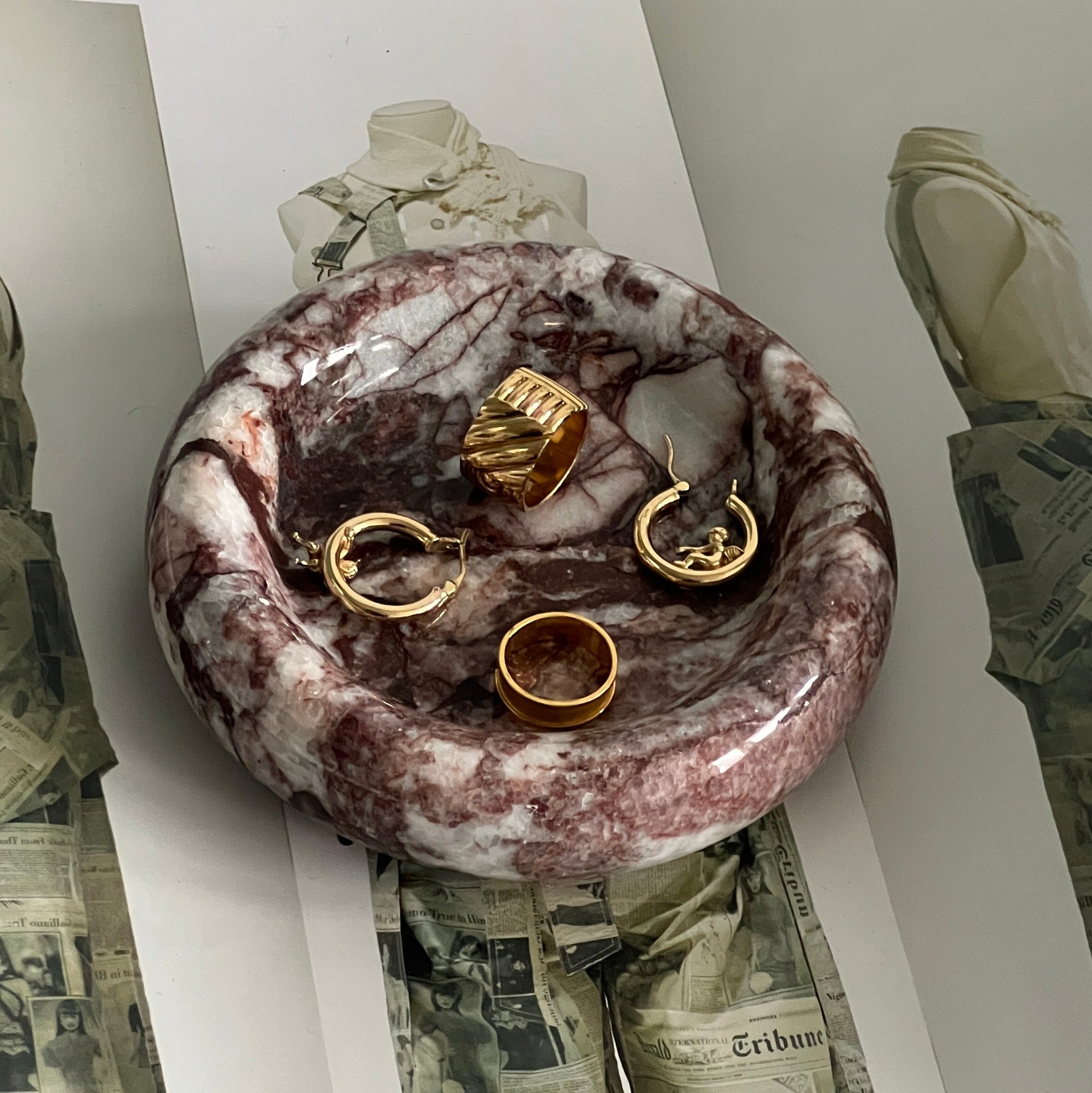 Marble-patterned jewelry dish with gold rings and pendants on a newspaper background