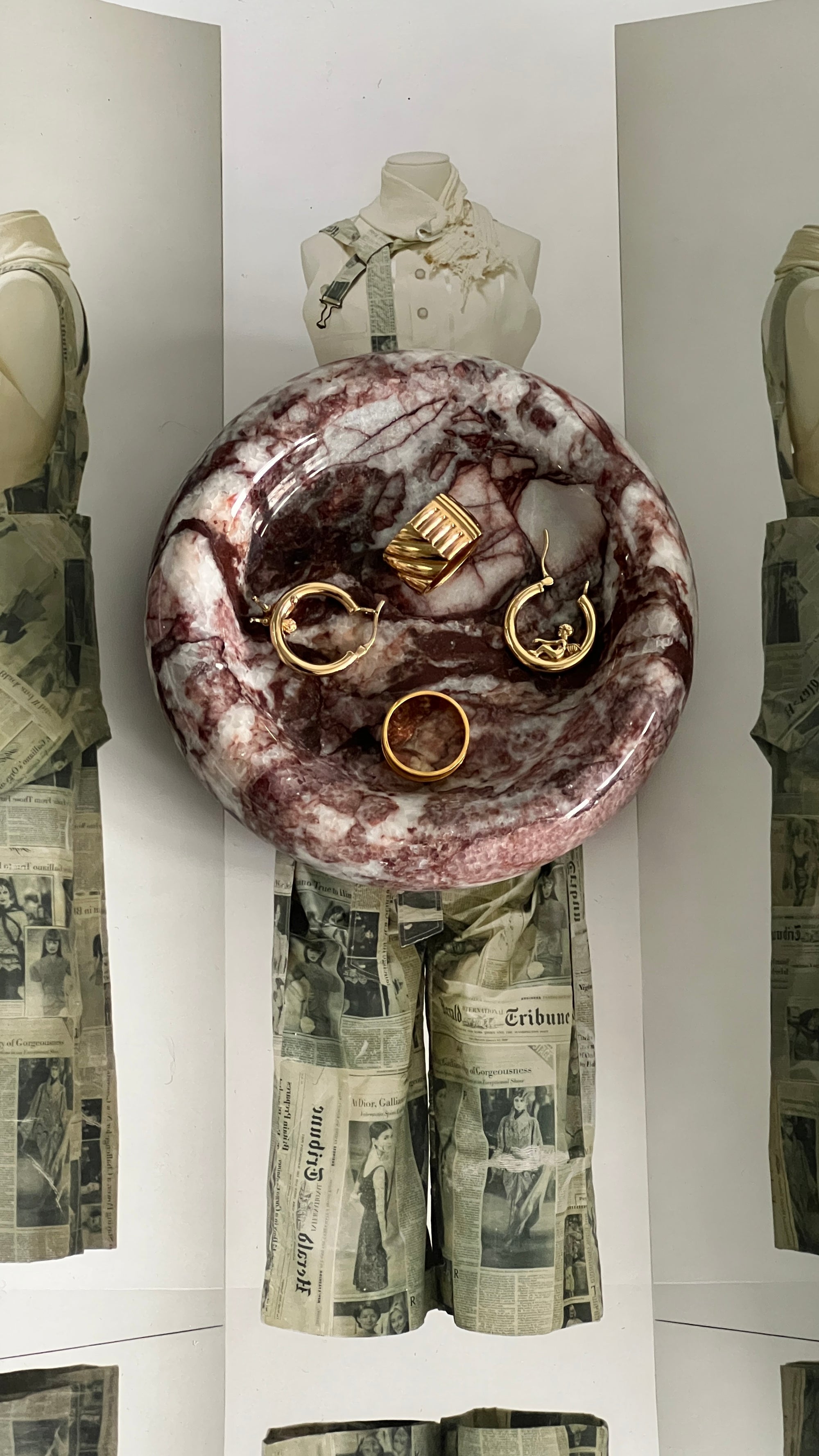 Marble-patterned dish with gold jewelry on a mannequin wearing a newspaper skirt.