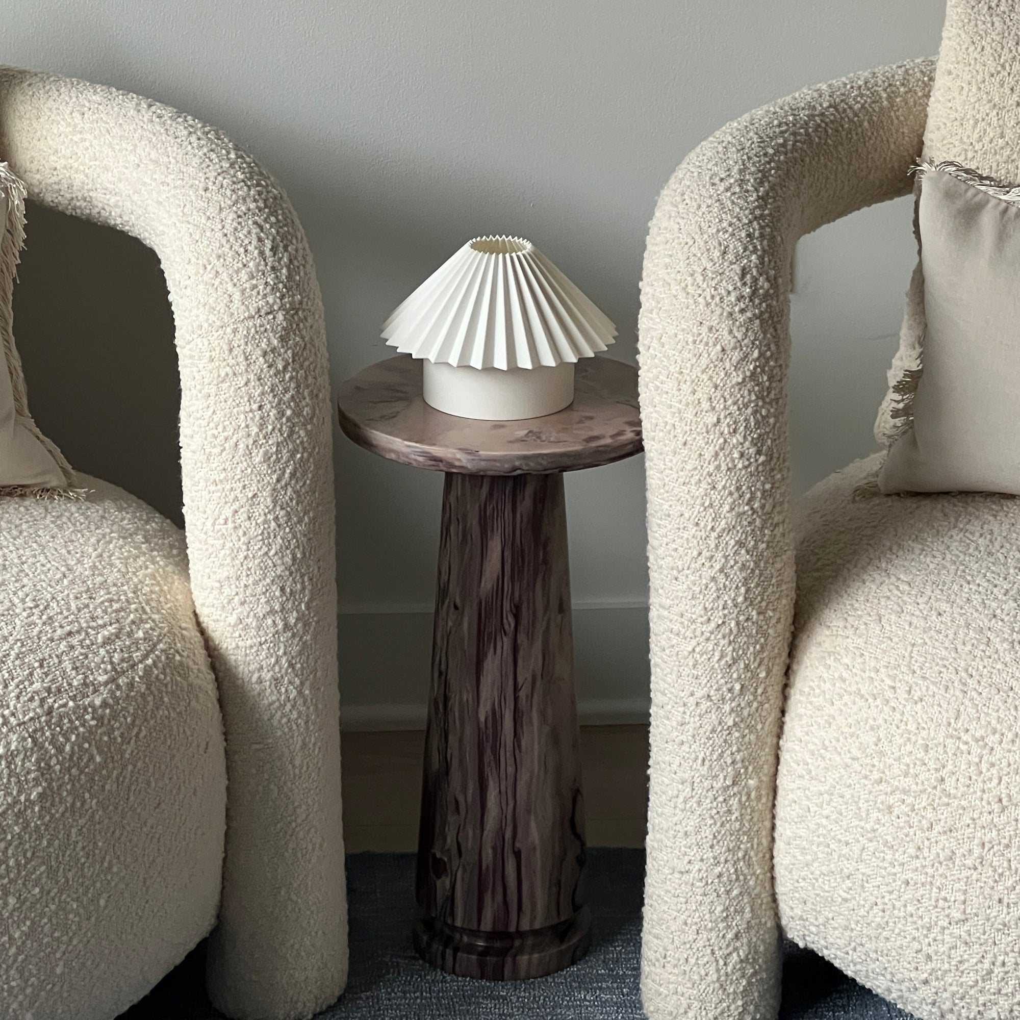 Two textured armchairs with a small round table and decorative lamp against a gray wall.