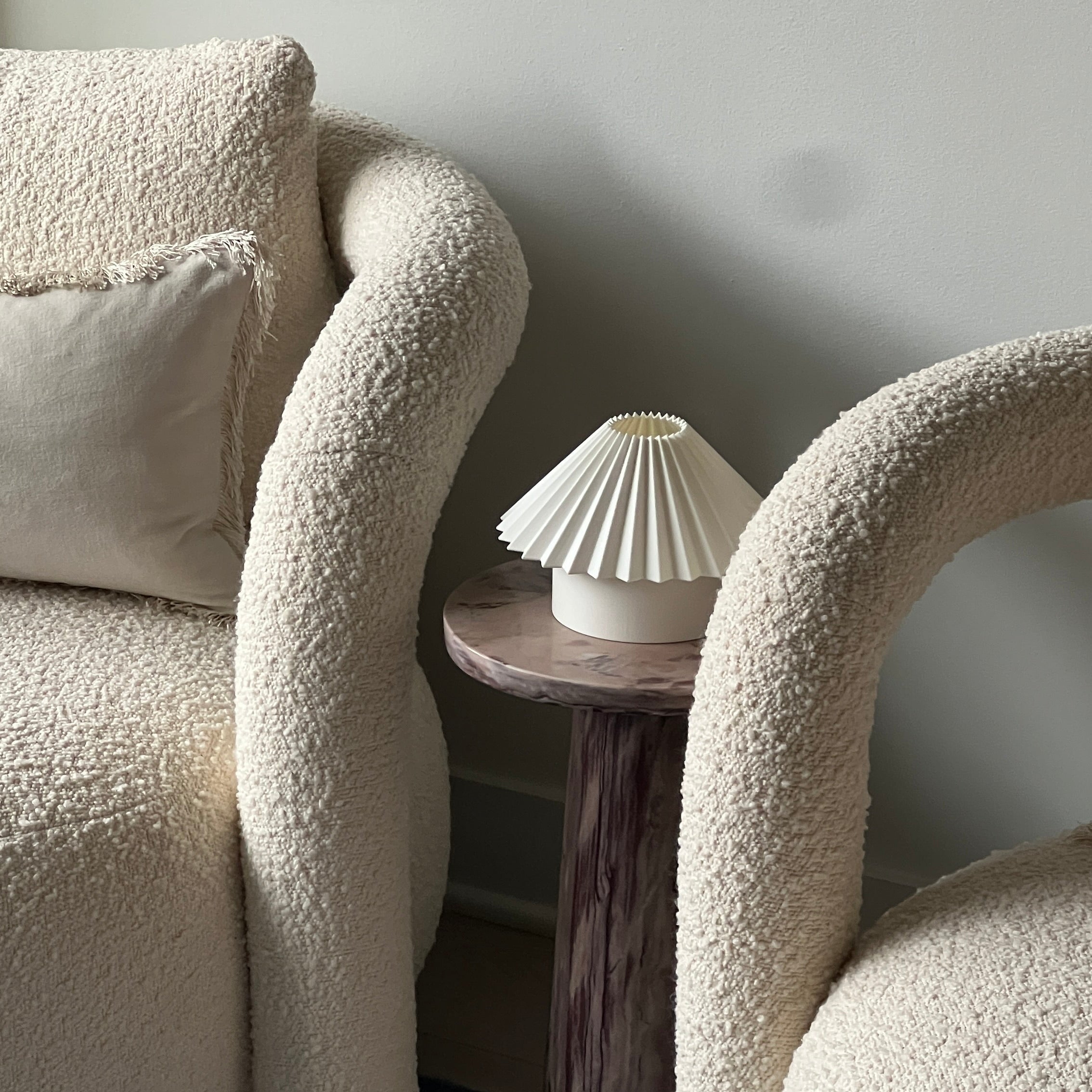 Two textured armchairs with a small round table between them against a plain wall.