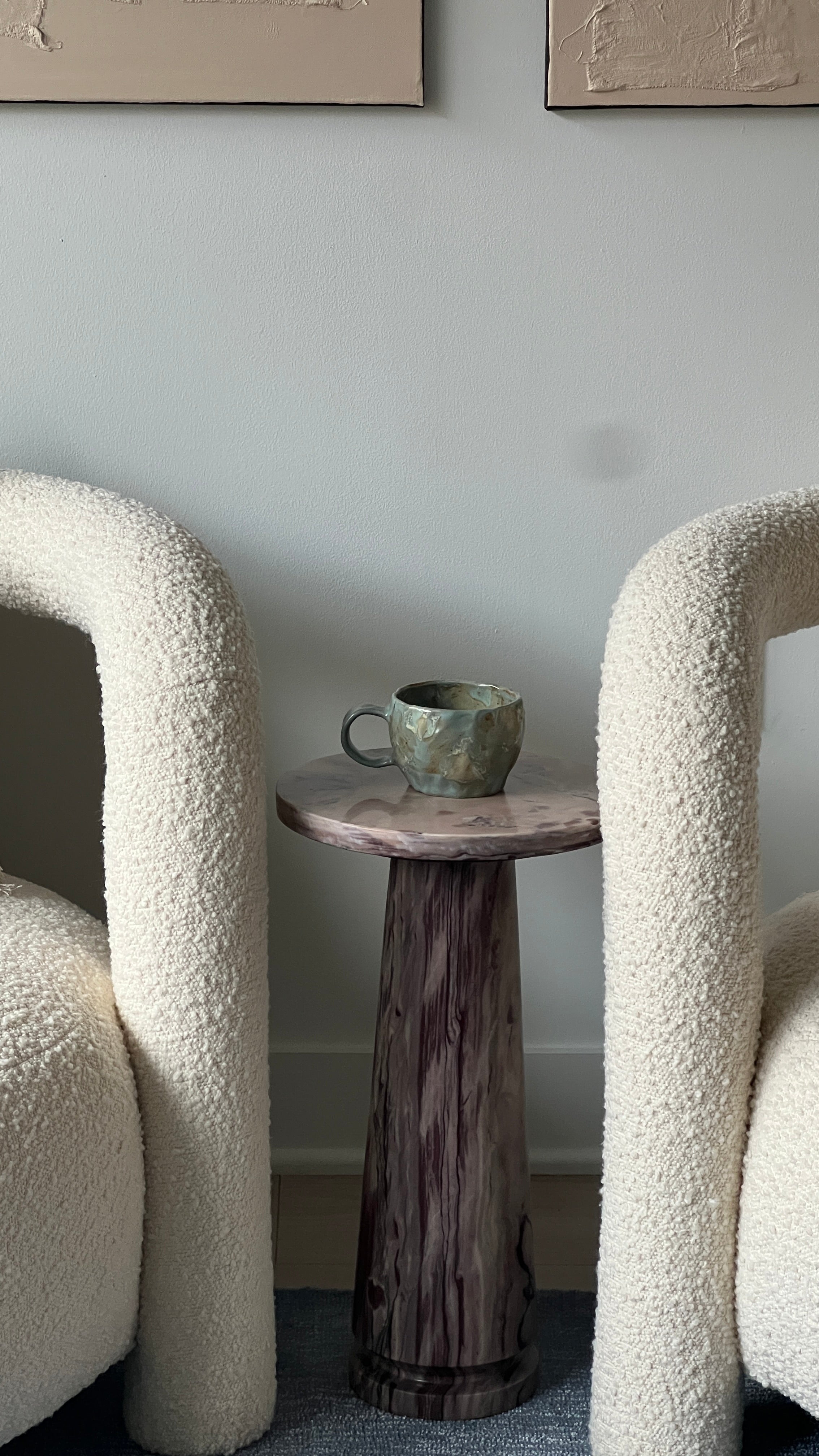 Two textured chairs with a wooden side table and green mug against a light gray wall.