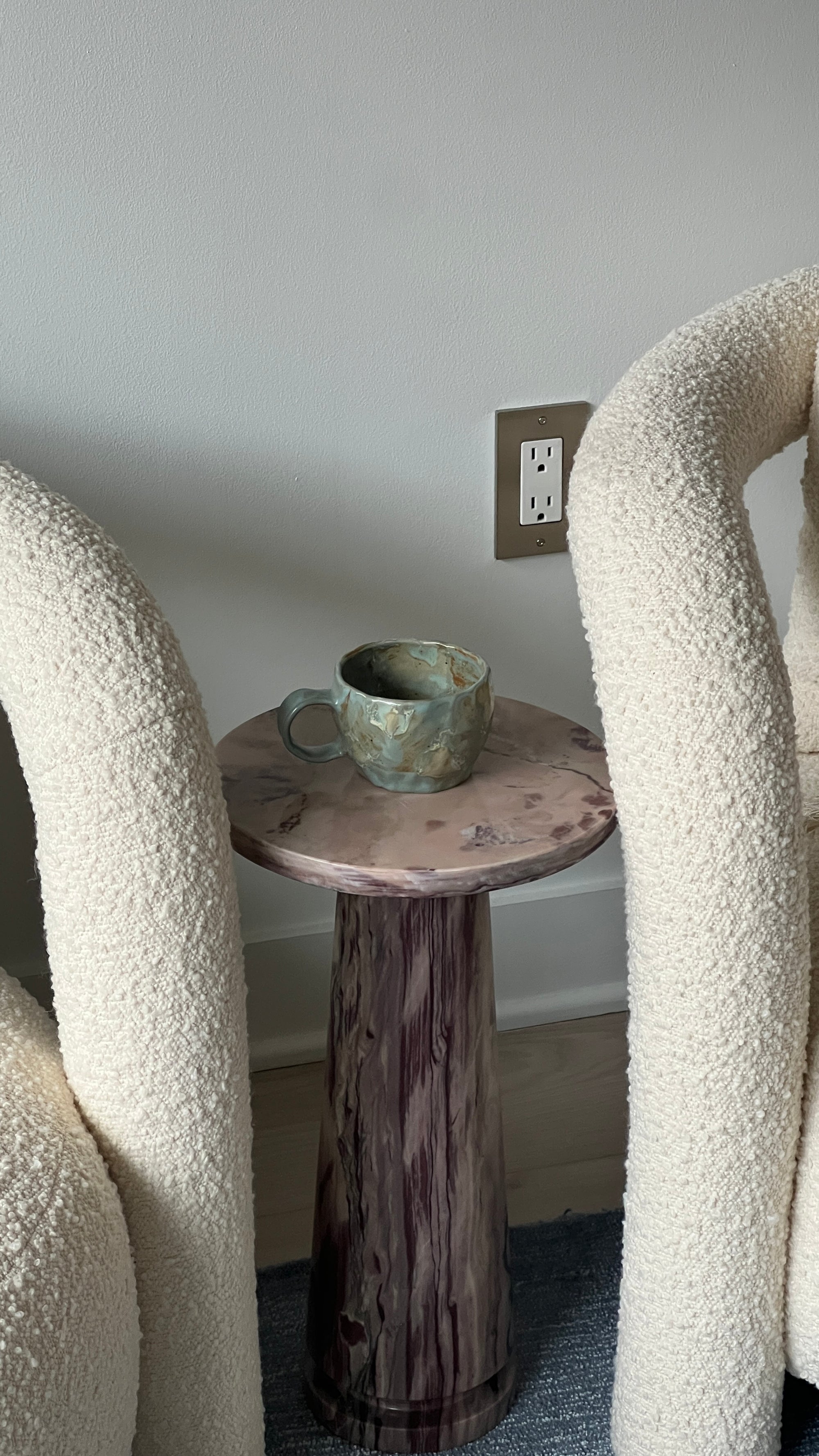 Small wooden side table with a green ceramic mug against a neutral wall.