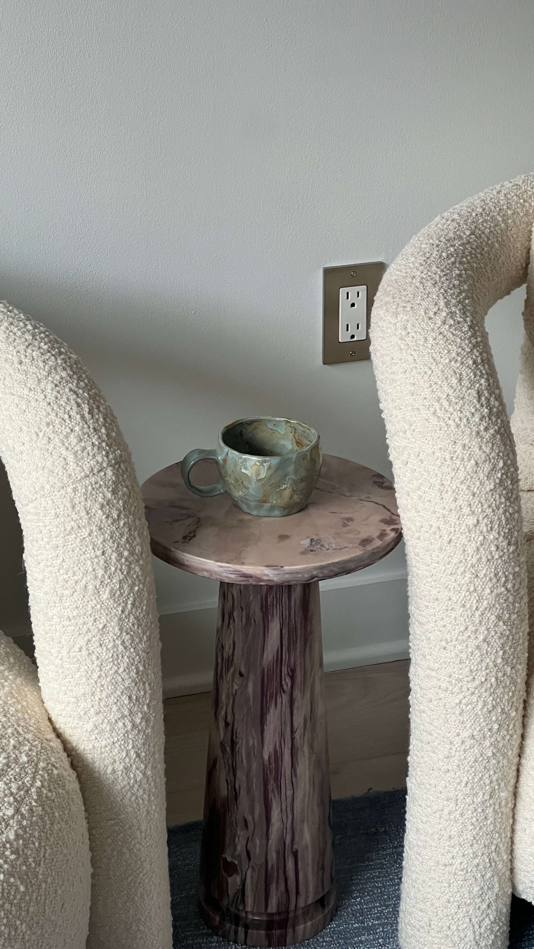 Small wooden side table with a green ceramic mug against a neutral wall.