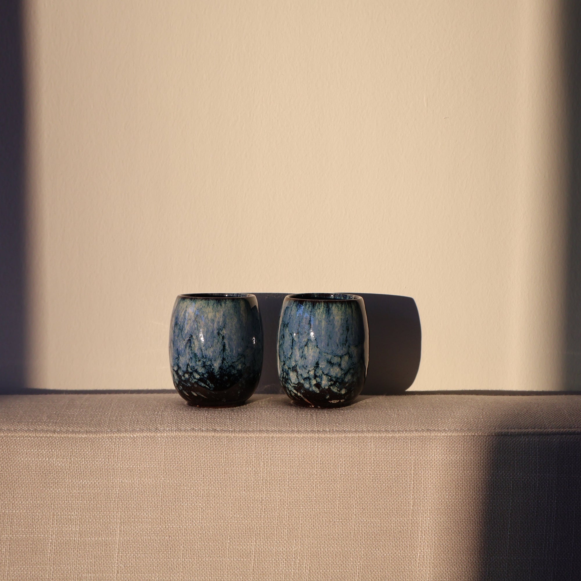 Two blue ceramic espresso cups on a beige surface with a neutral background