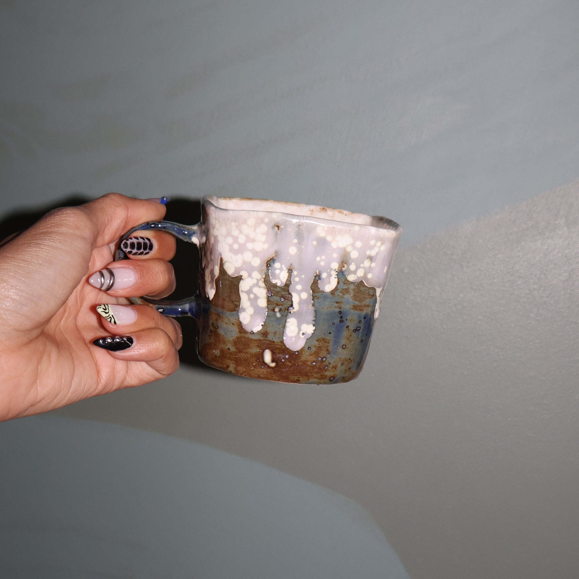 Hand holding a ceramic mug against a green wall