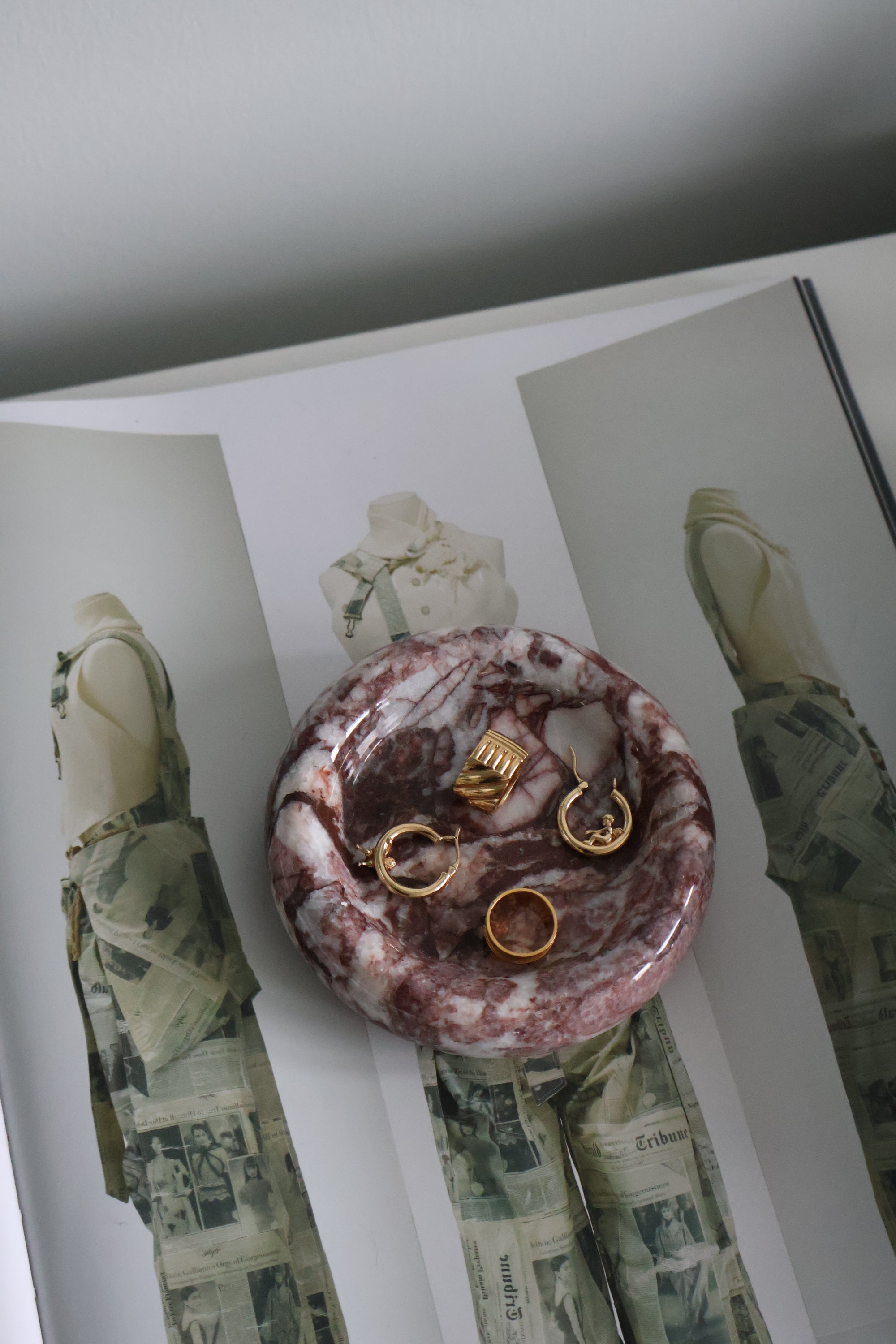 Marble-patterned jewelry dish with gold rings on a magazine background