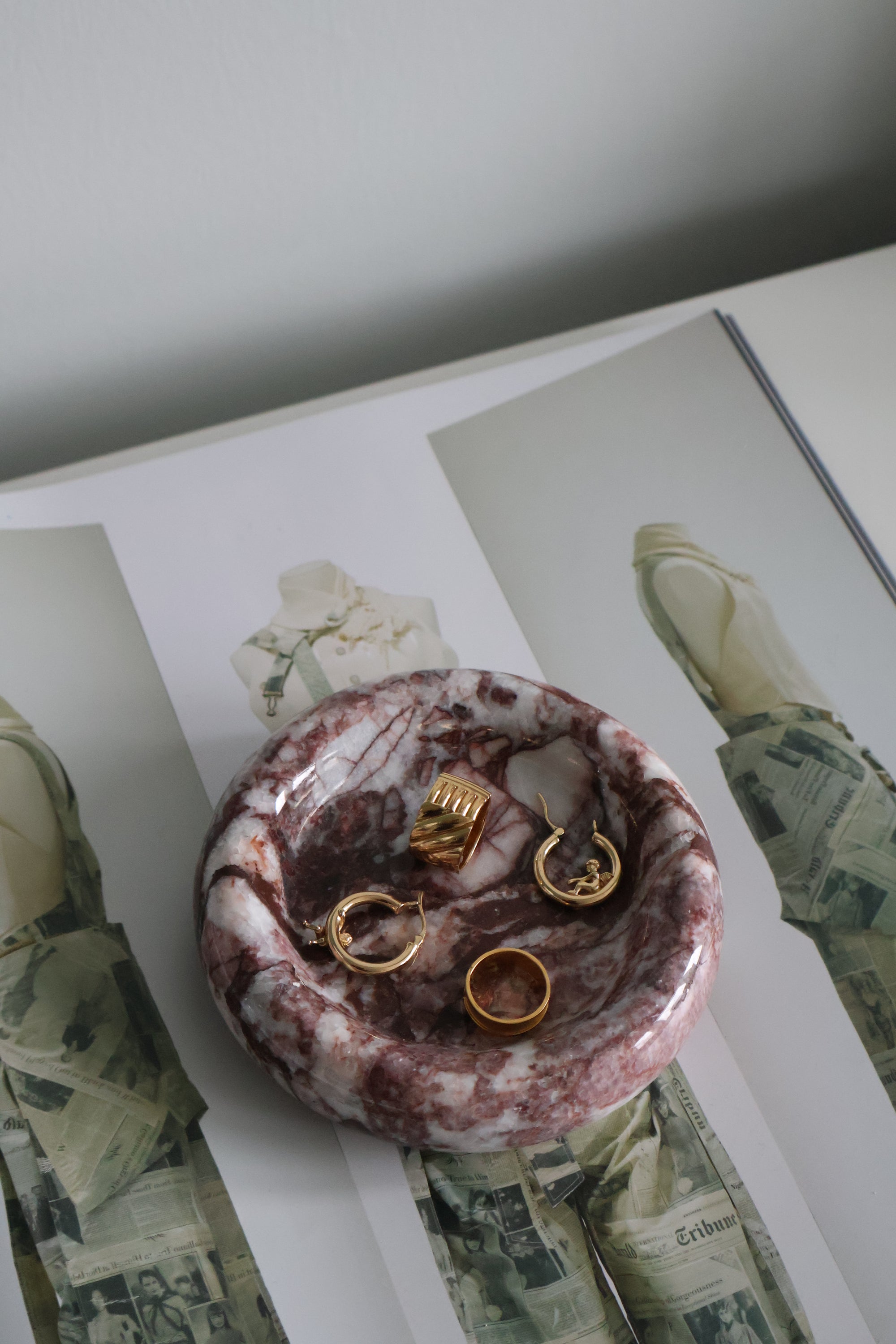 Marble-patterned jewelry dish with gold rings on a magazine background