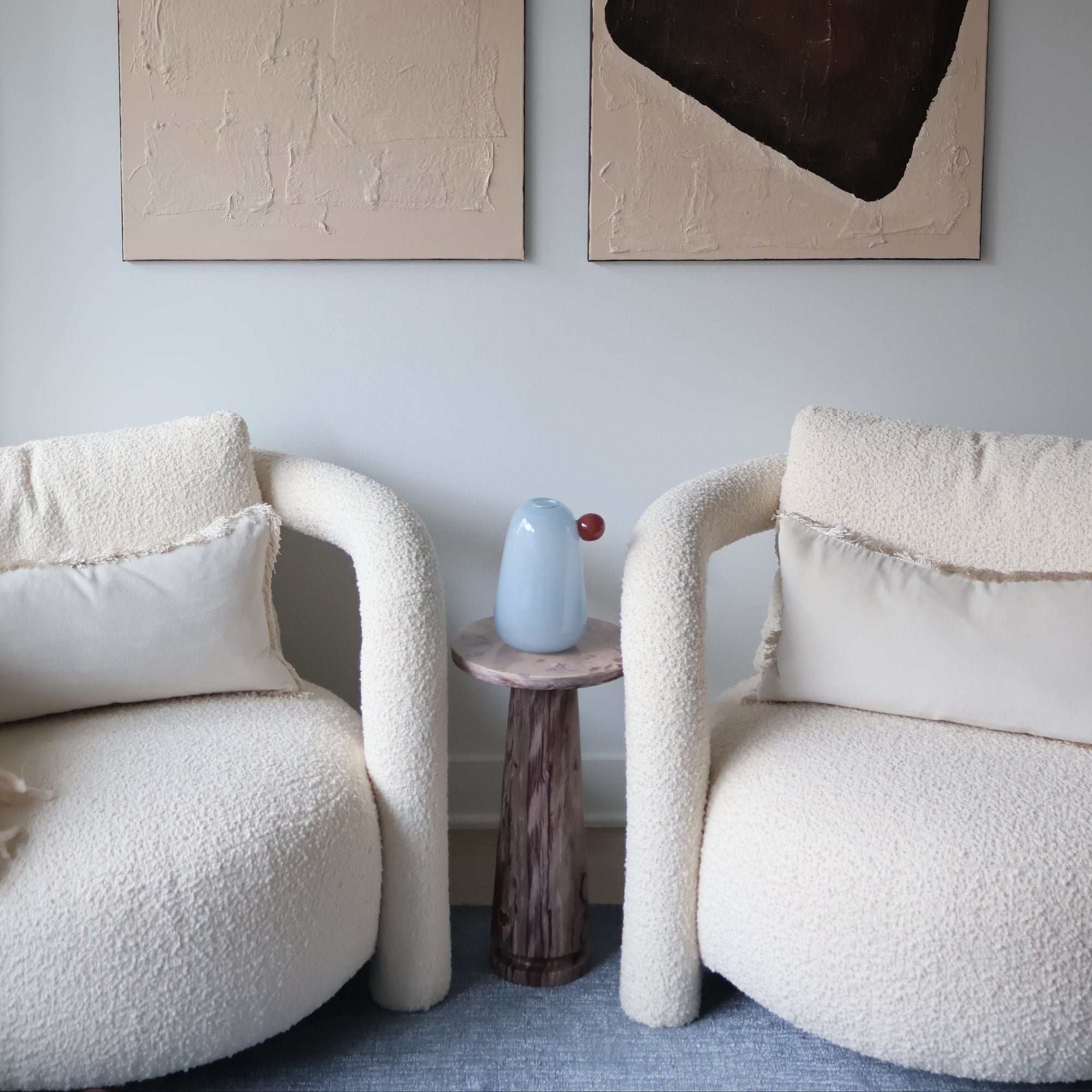 Two abstract paintings on a wall with a modern chair and decorative items.