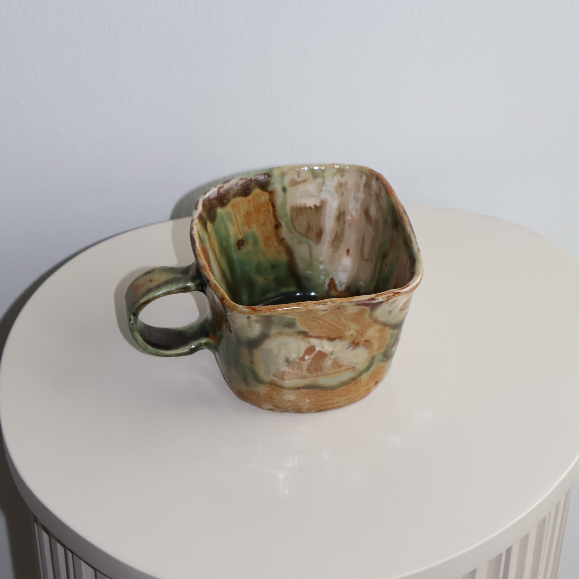 Rust-colored ceramic cup on a white cylindrical object with a ribbed texture.