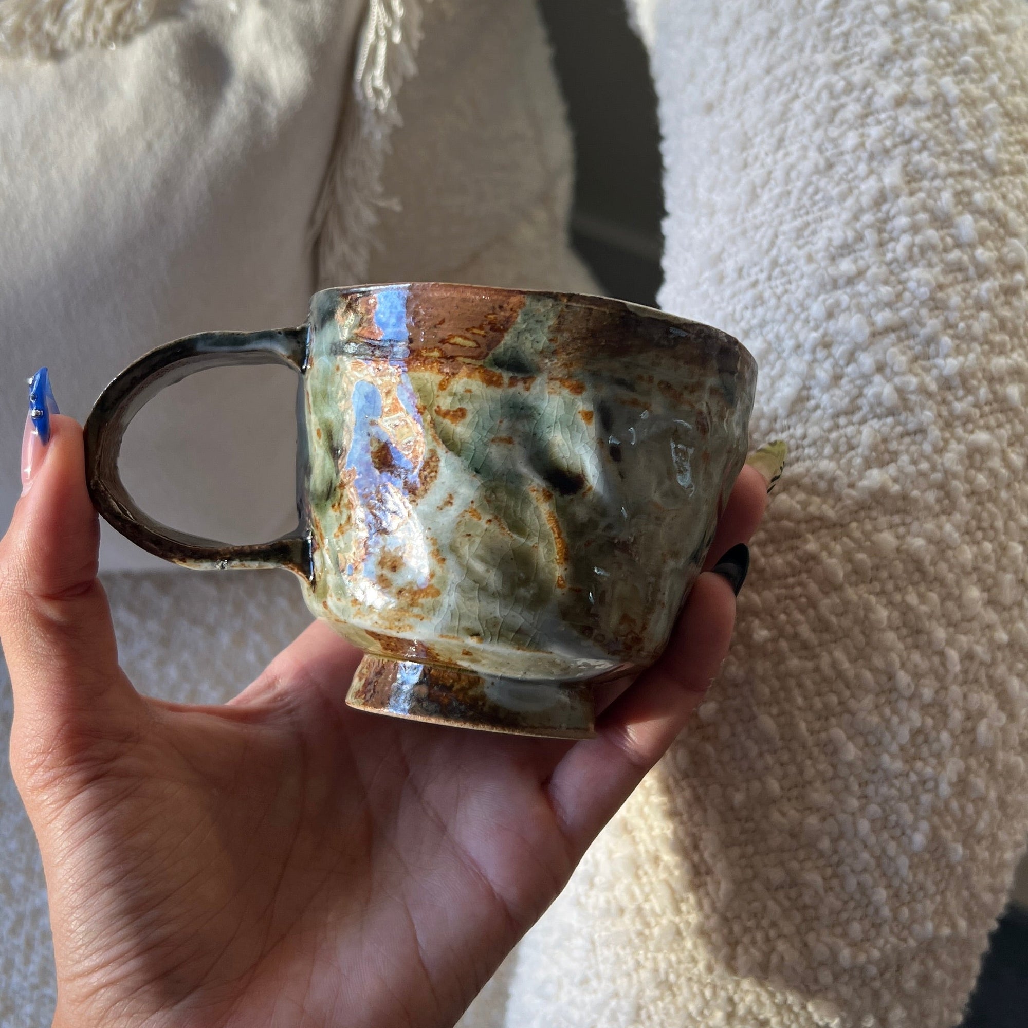 Hand holding a ceramic mug with a textured surface against a soft, neutral background