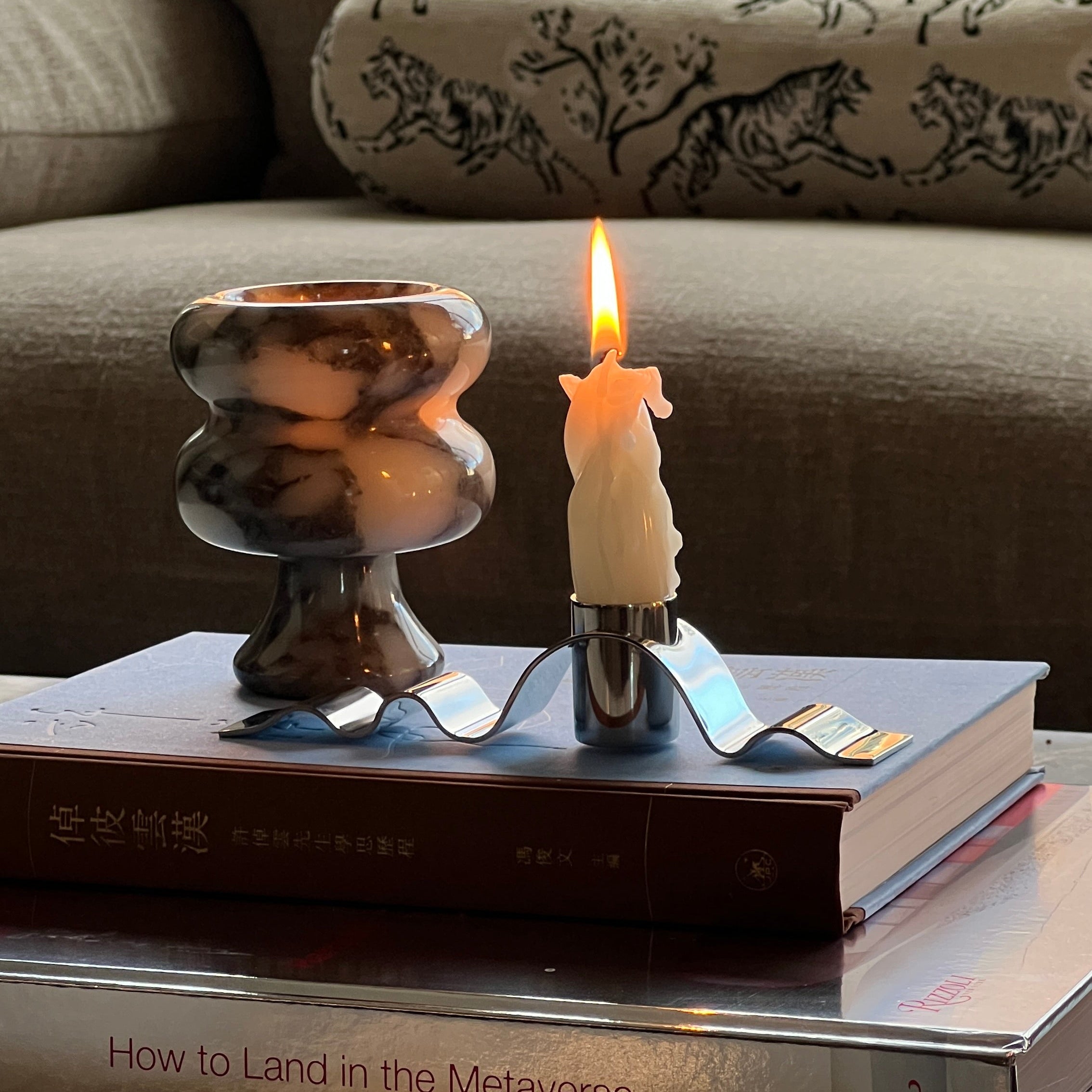 Candle burning on a stack of books with a couch and window in the background