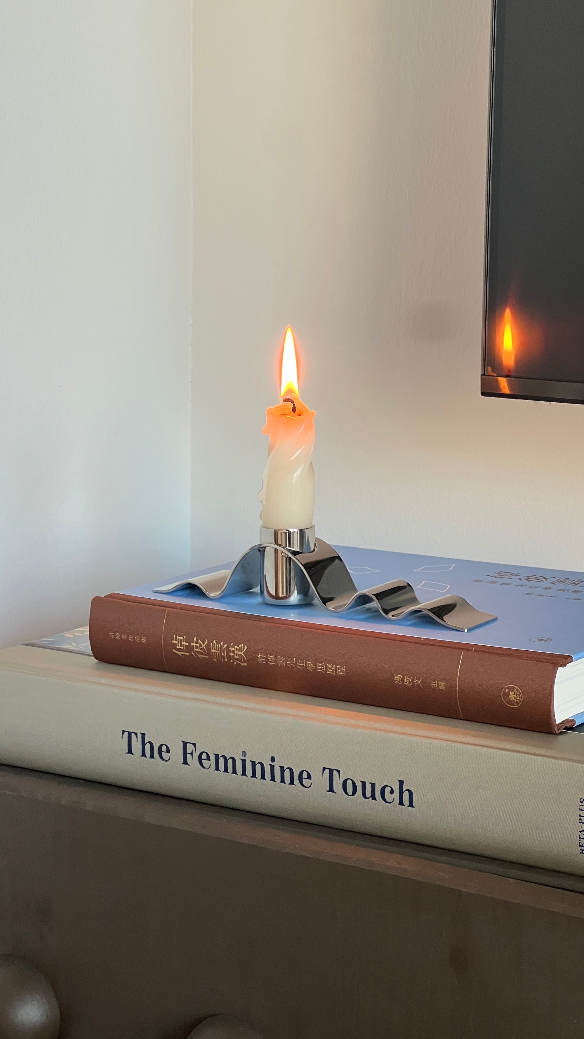 Candle on top of books titled 'The Feminine Touch' with a blurred background