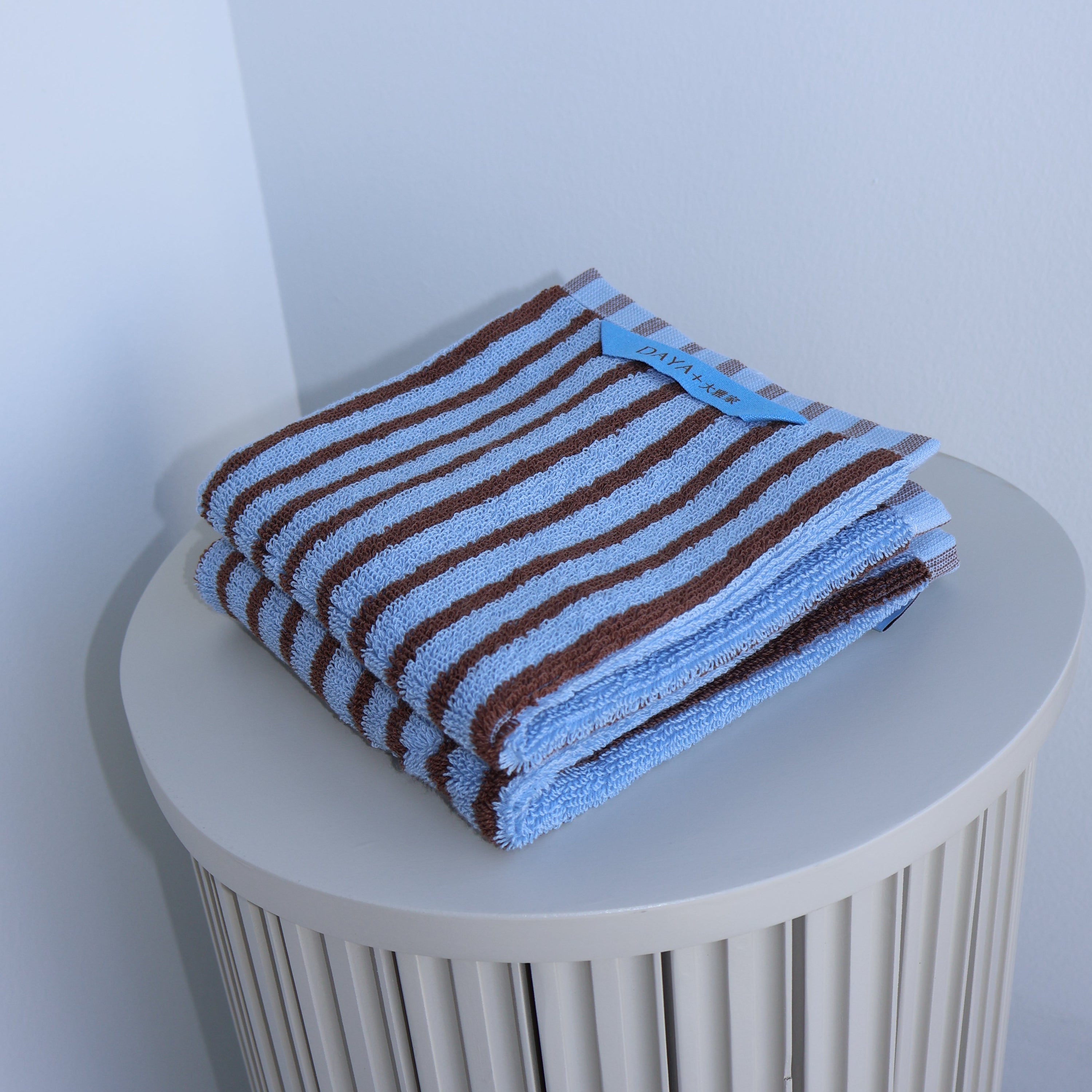 Striped blue and brown towel on a cylindrical white holder against a light gray background