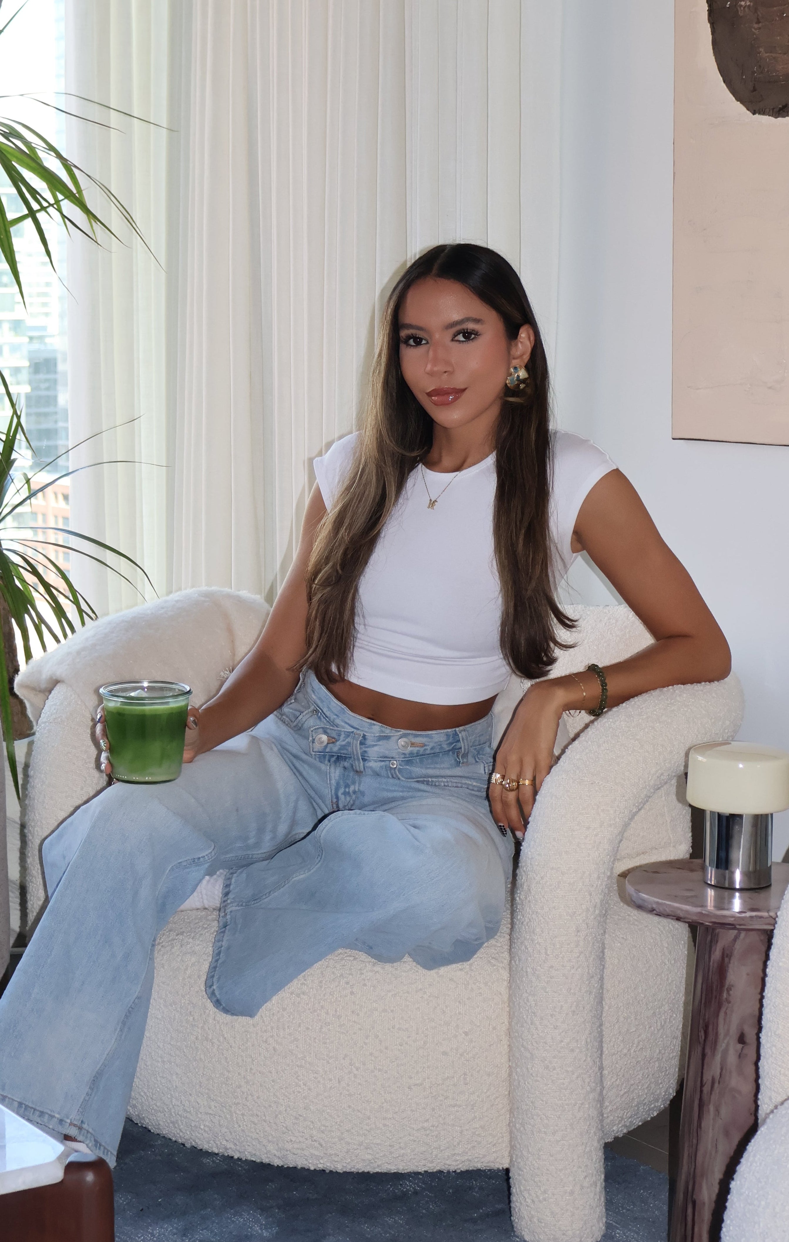 Woman sitting on a couch in a modern living room with plants and a cityscape view.