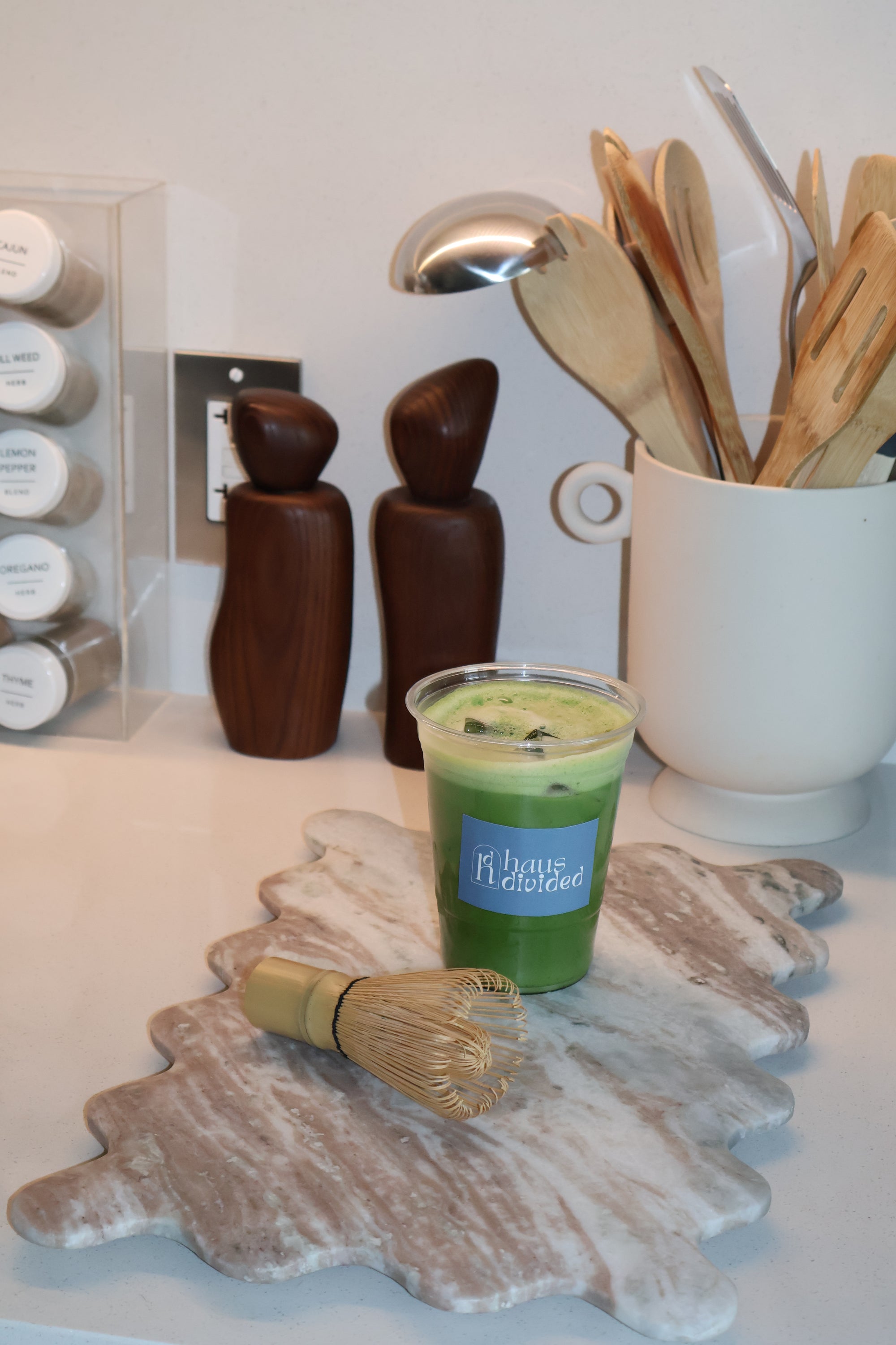 Set of wooden utensils, a container of matcha powder, and a bamboo whisk on a white surface.